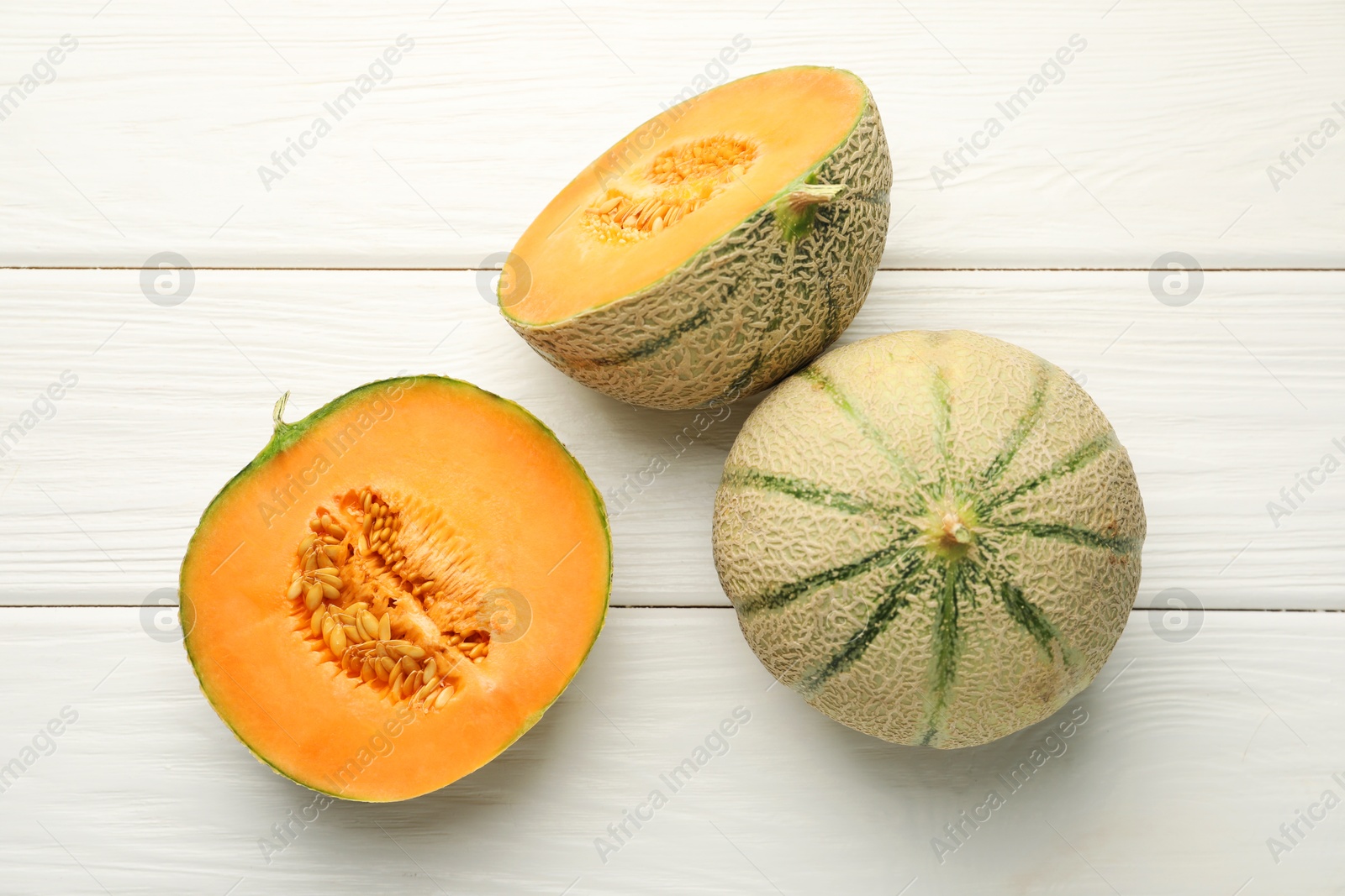 Photo of Whole and cut ripe Cantaloupe melons on white wooden table, flat lay