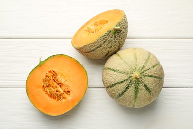 Photo of Whole and cut ripe Cantaloupe melons on white wooden table, flat lay