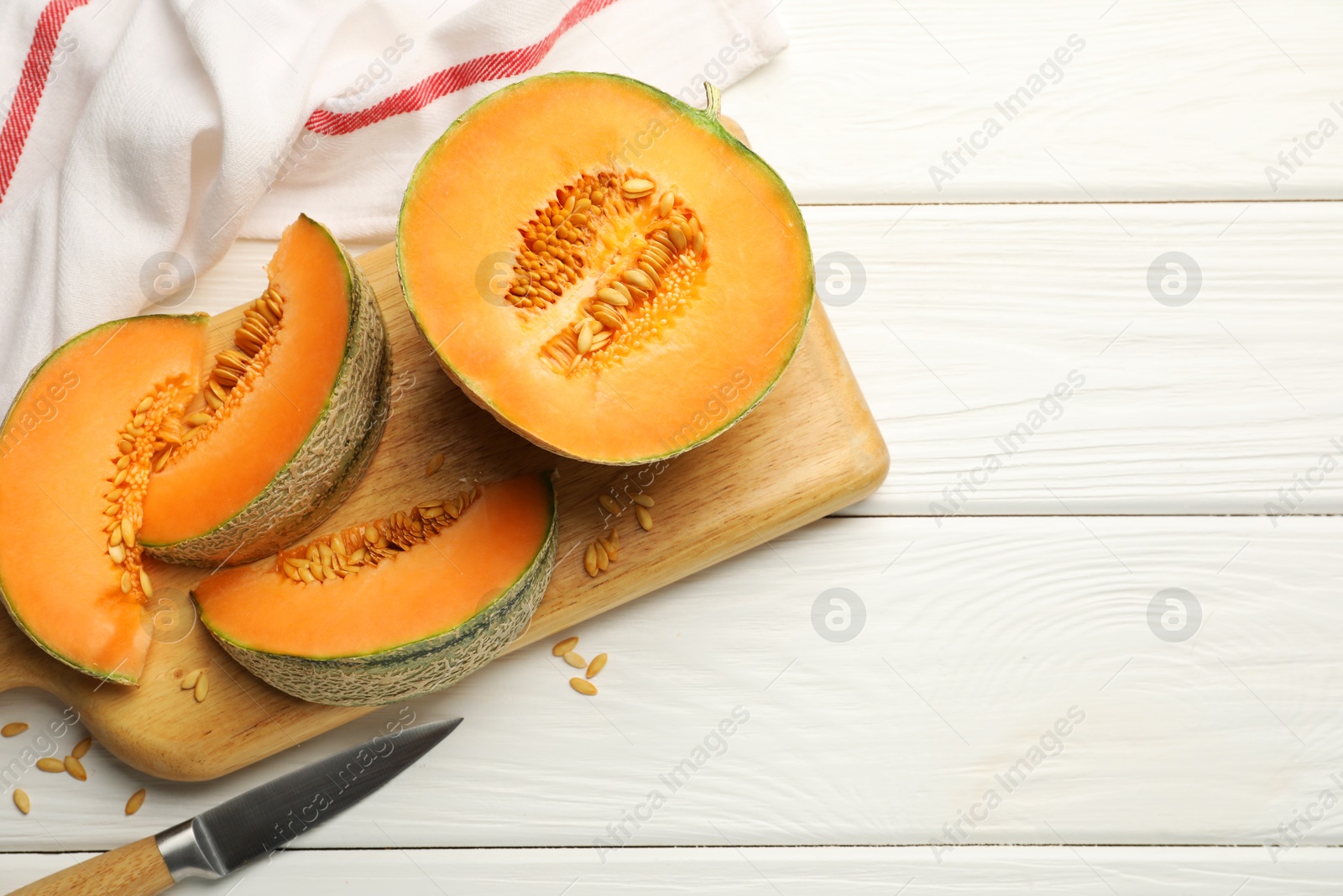 Photo of Cut ripe Cantaloupe melon and knife on white wooden table, flat lay. Space for text