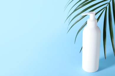 Shampoo in bottle and green palm leaves on light blue background. Space for text