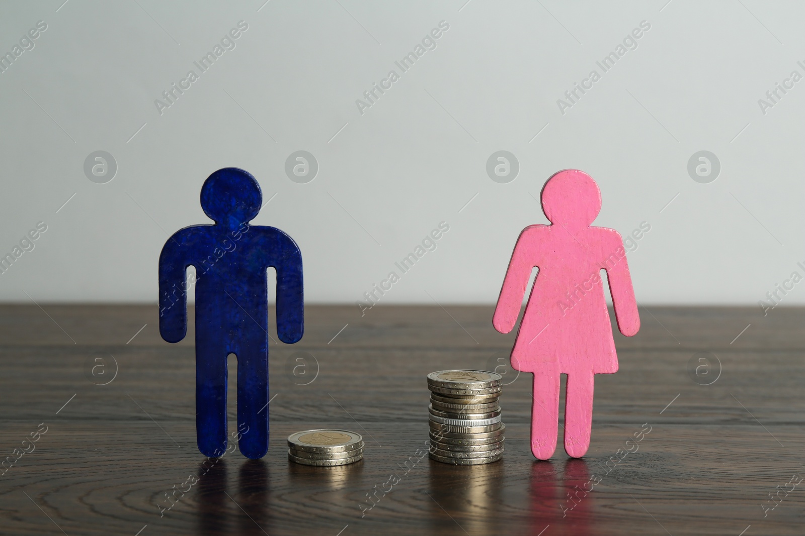 Photo of Financial inequality. Male and female figures with uneven amount of coins on wooden table