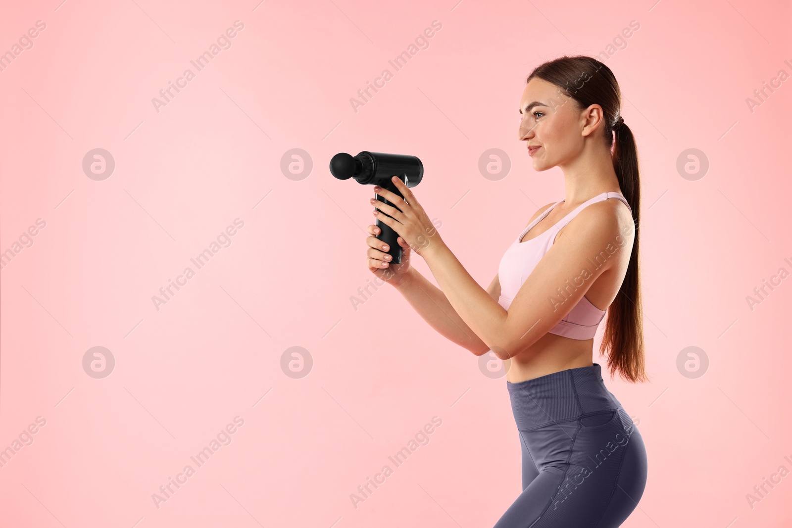 Photo of Young woman with percussive massager on pink background. Space for text