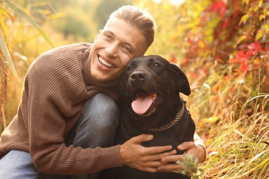 Smiling man hugging cute dog outdoors on autumn day