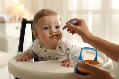 Mother feeding her cute little baby in high chair at home, closeup