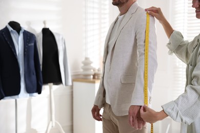 Woman measuring sleeve on man in atelier, closeup