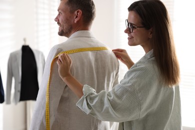 Photo of Woman measuring man's shoulders with tape in atelier