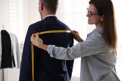 Tailor measuring jacket on man during fitting in atelier, closeup