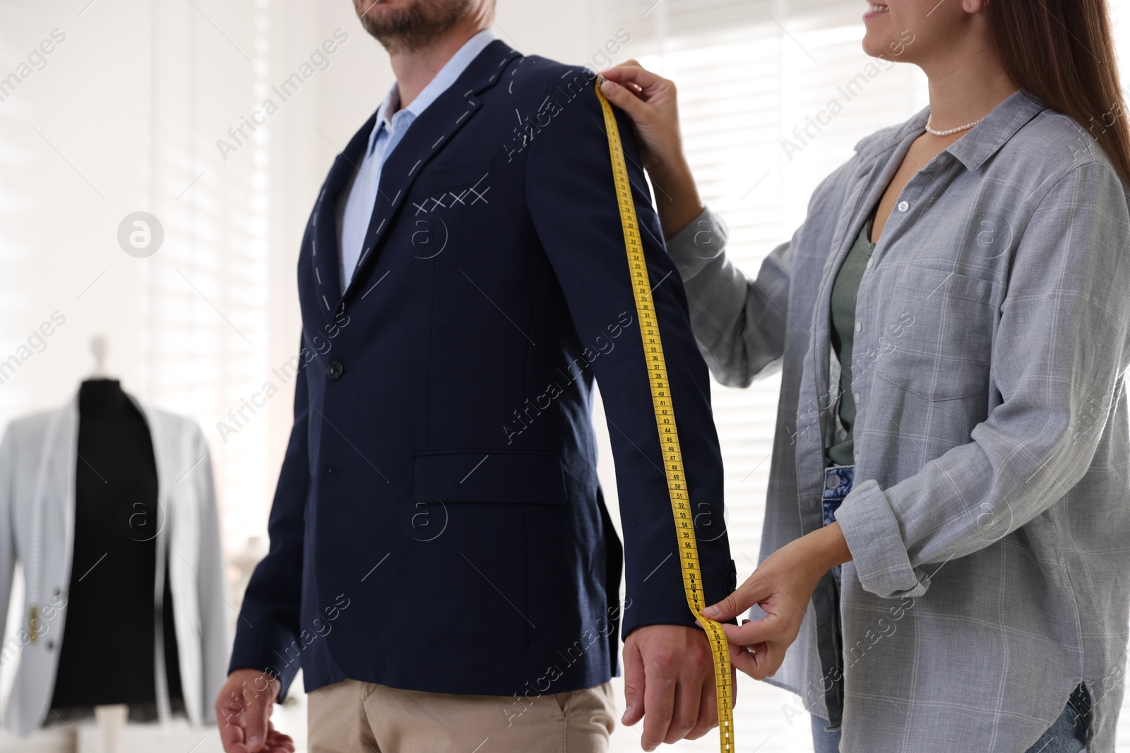 Photo of Tailor measuring jacket on man during fitting in atelier, closeup