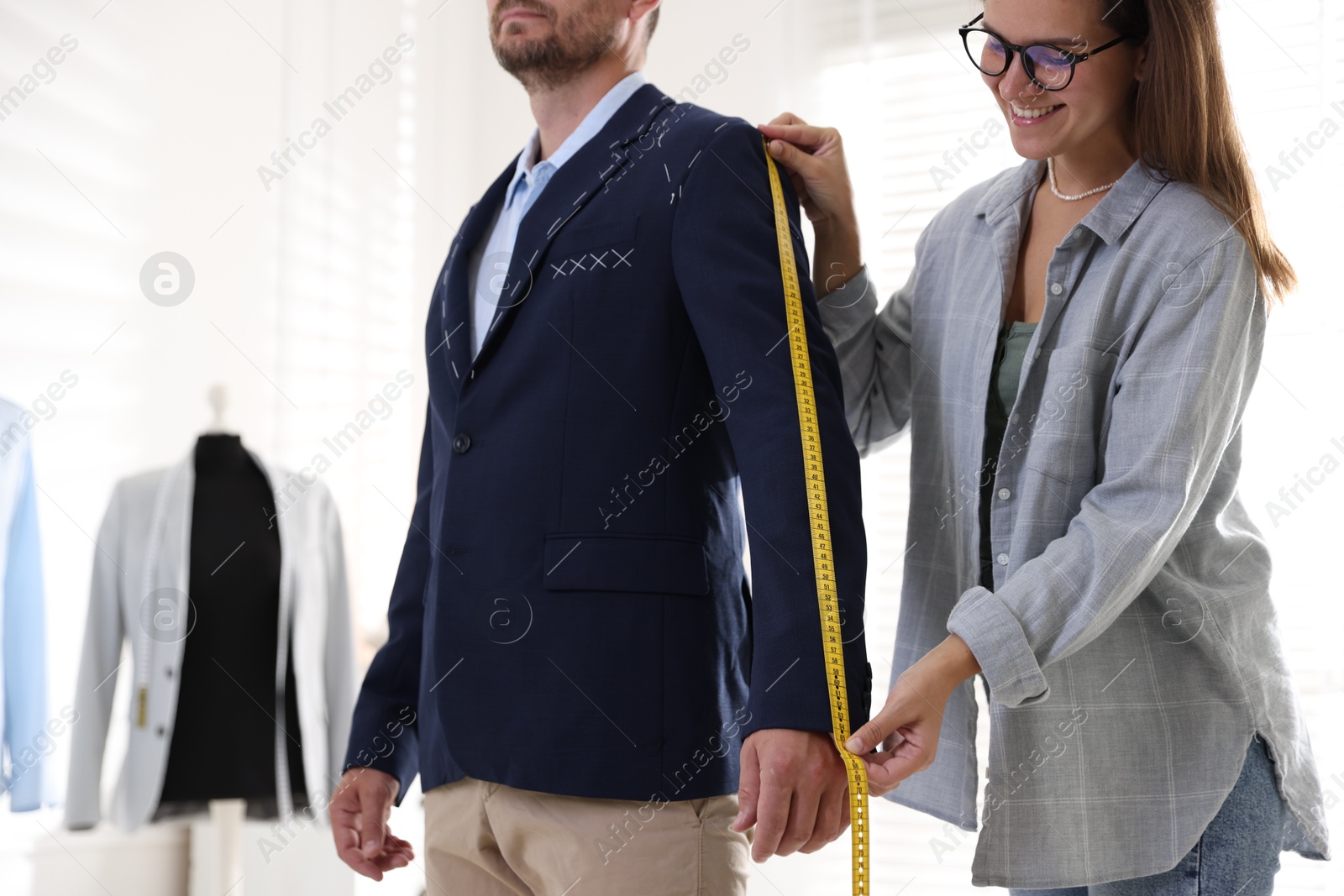 Photo of Tailor measuring jacket on man during fitting in atelier, closeup