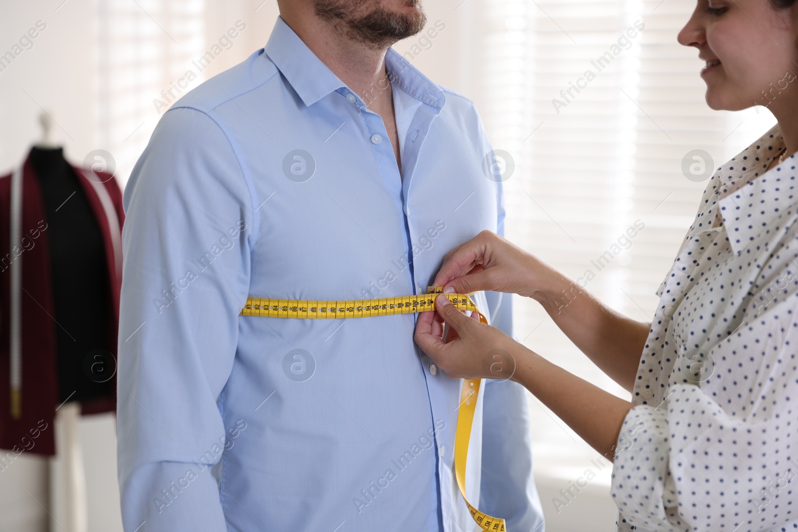 Photo of Woman measuring man's chest with tape in atelier