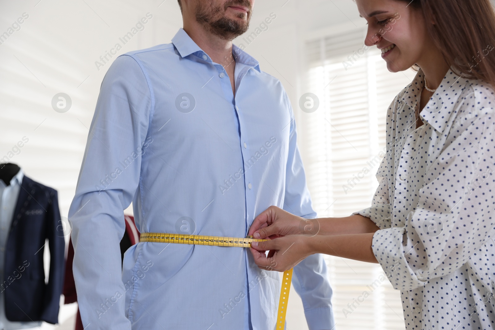 Photo of Woman measuring man's waist with tape in atelier