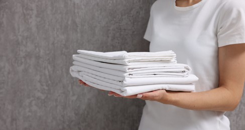 Photo of Woman with clean bed linens near grey wall, closeup. Space for text