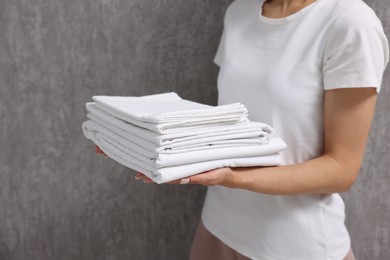 Woman with clean bed linens near grey wall, closeup