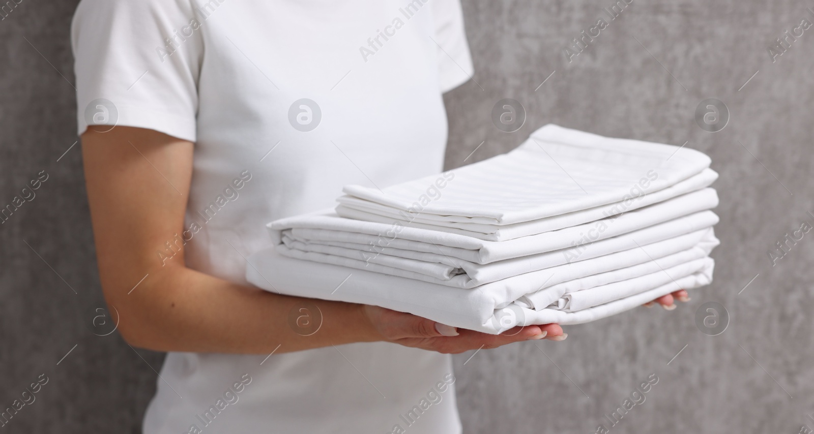 Photo of Woman with clean bed linens near grey wall, closeup