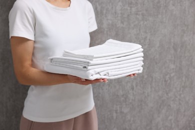 Woman with clean bed linens near grey wall, closeup