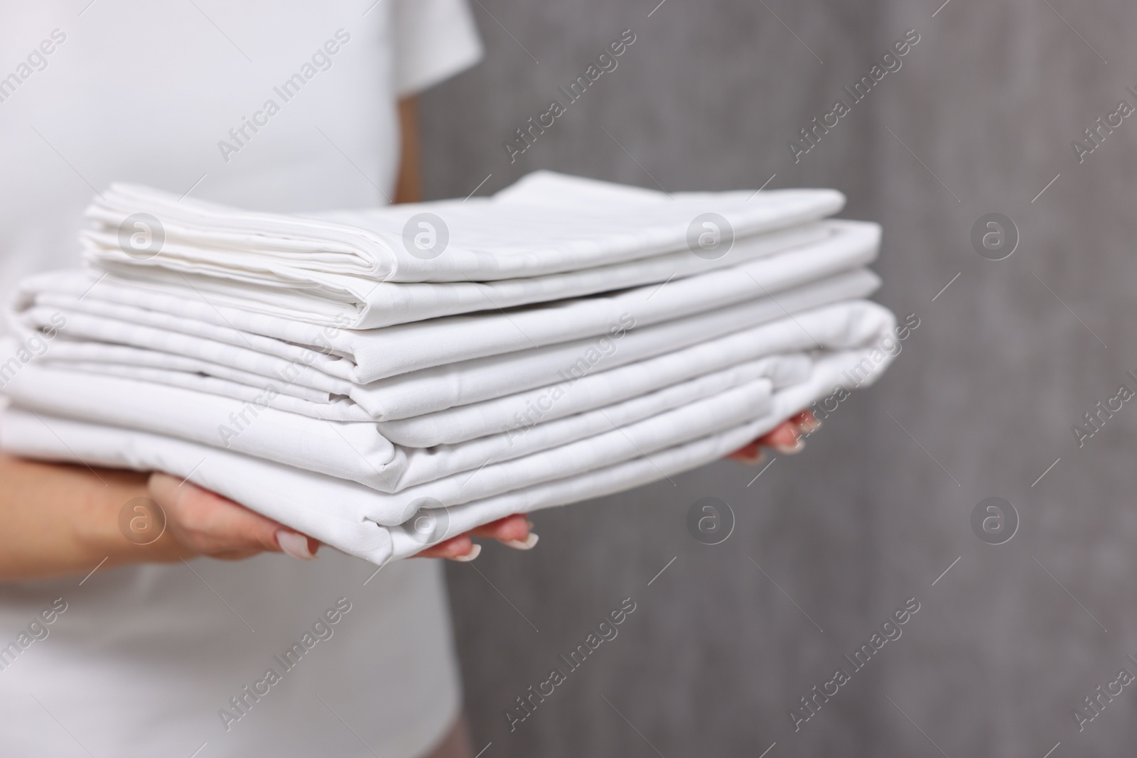 Photo of Woman with clean bed linens near grey wall, closeup