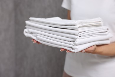 Woman with clean bed linens near grey wall, closeup