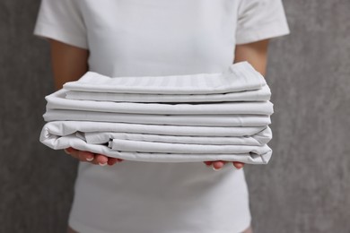 Photo of Woman with clean bed linens near grey wall, closeup