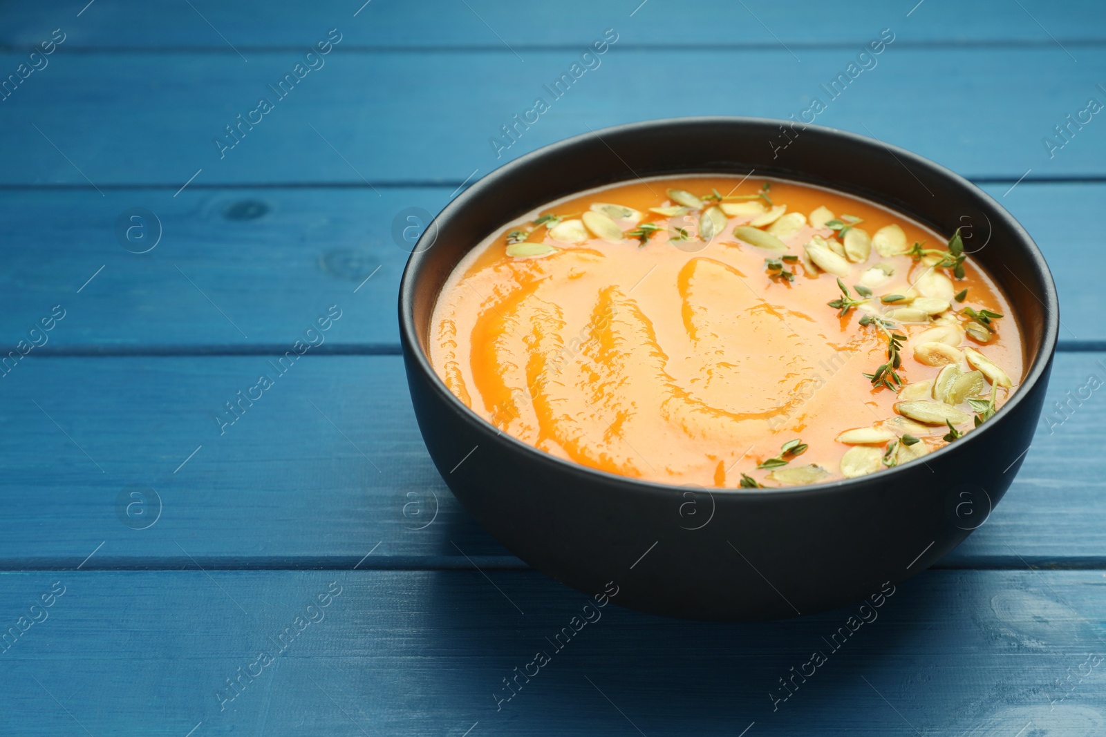 Photo of Delicious sweet potato soup with pumpkin seeds in bowl on blue wooden table, closeup. Space for text