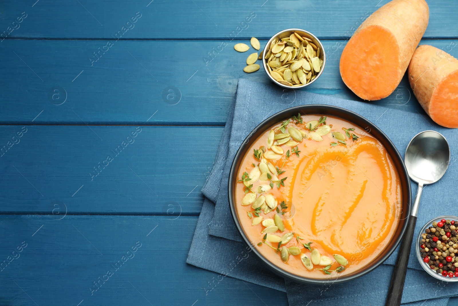 Photo of Delicious sweet potato soup with pumpkin seeds served on blue wooden table, flat lay. Space for text