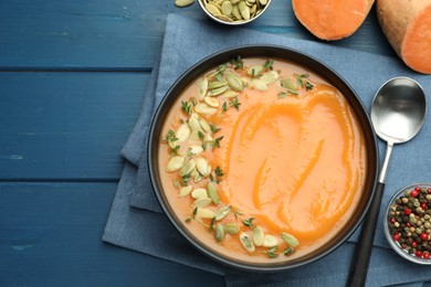 Photo of Delicious sweet potato soup with pumpkin seeds served on blue wooden table, flat lay