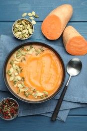 Photo of Delicious sweet potato soup with pumpkin seeds served on blue wooden table, flat lay