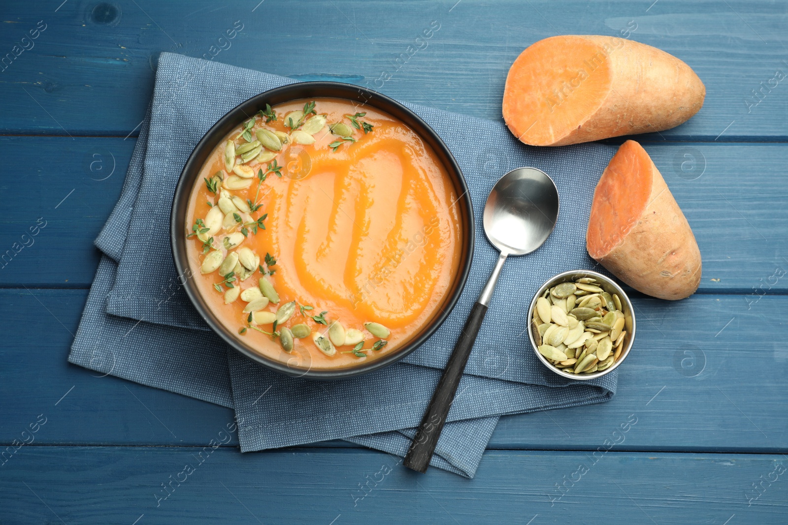 Delicious sweet potato soup with pumpkin seeds served on blue wooden table, flat lay Photo of Delicious sweet potato soup with pumpkin seeds served on blue wooden table, flat lay