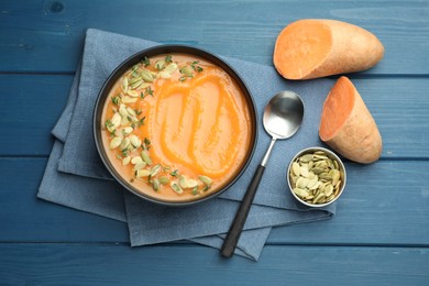 Photo of Delicious sweet potato soup with pumpkin seeds served on blue wooden table, flat lay