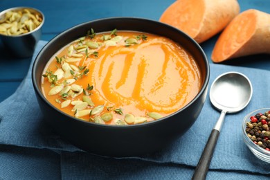 Photo of Delicious sweet potato soup with pumpkin seeds served on blue wooden table, closeup