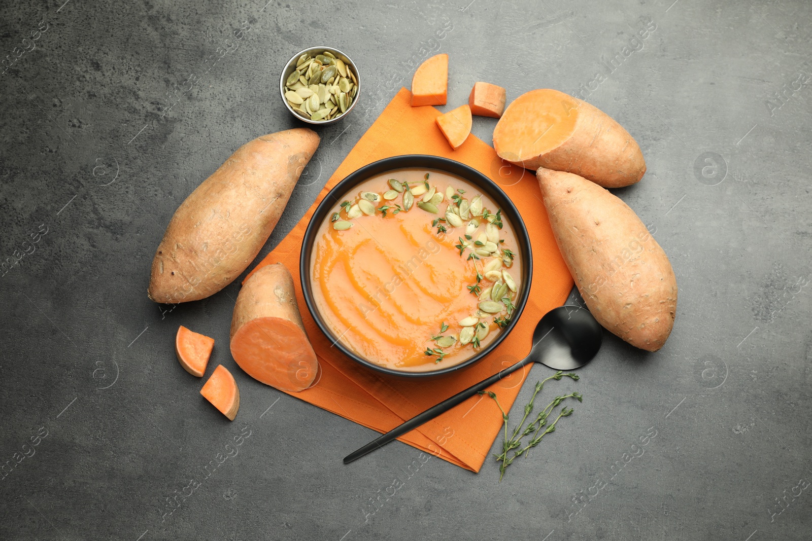 Photo of Delicious sweet potato soup with pumpkin seeds in bowl and vegetables on grey table, flat lay