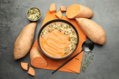 Photo of Delicious sweet potato soup with pumpkin seeds in bowl and vegetables on grey table, flat lay