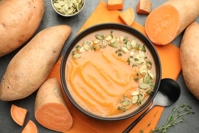 Photo of Delicious sweet potato soup with pumpkin seeds in bowl and vegetables on grey table, flat lay