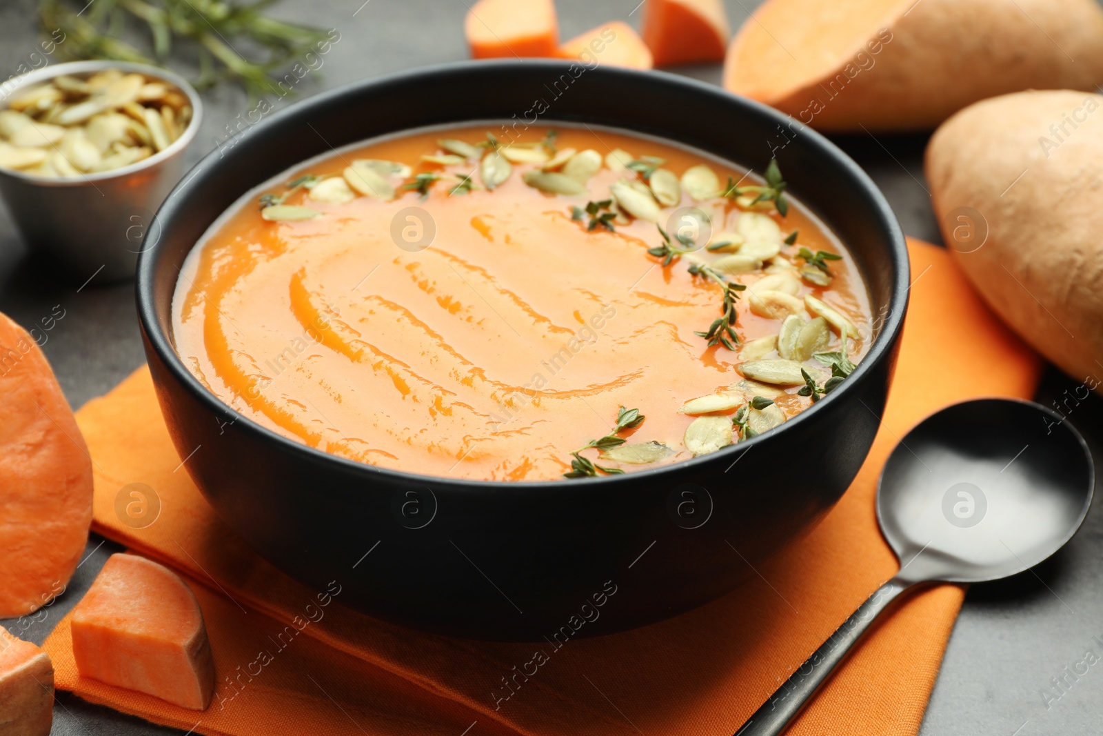 Photo of Delicious sweet potato soup with pumpkin seeds in bowl and vegetables on grey table, closeup