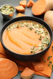 Photo of Delicious sweet potato soup with pumpkin seeds in bowl and vegetables on grey table, closeup