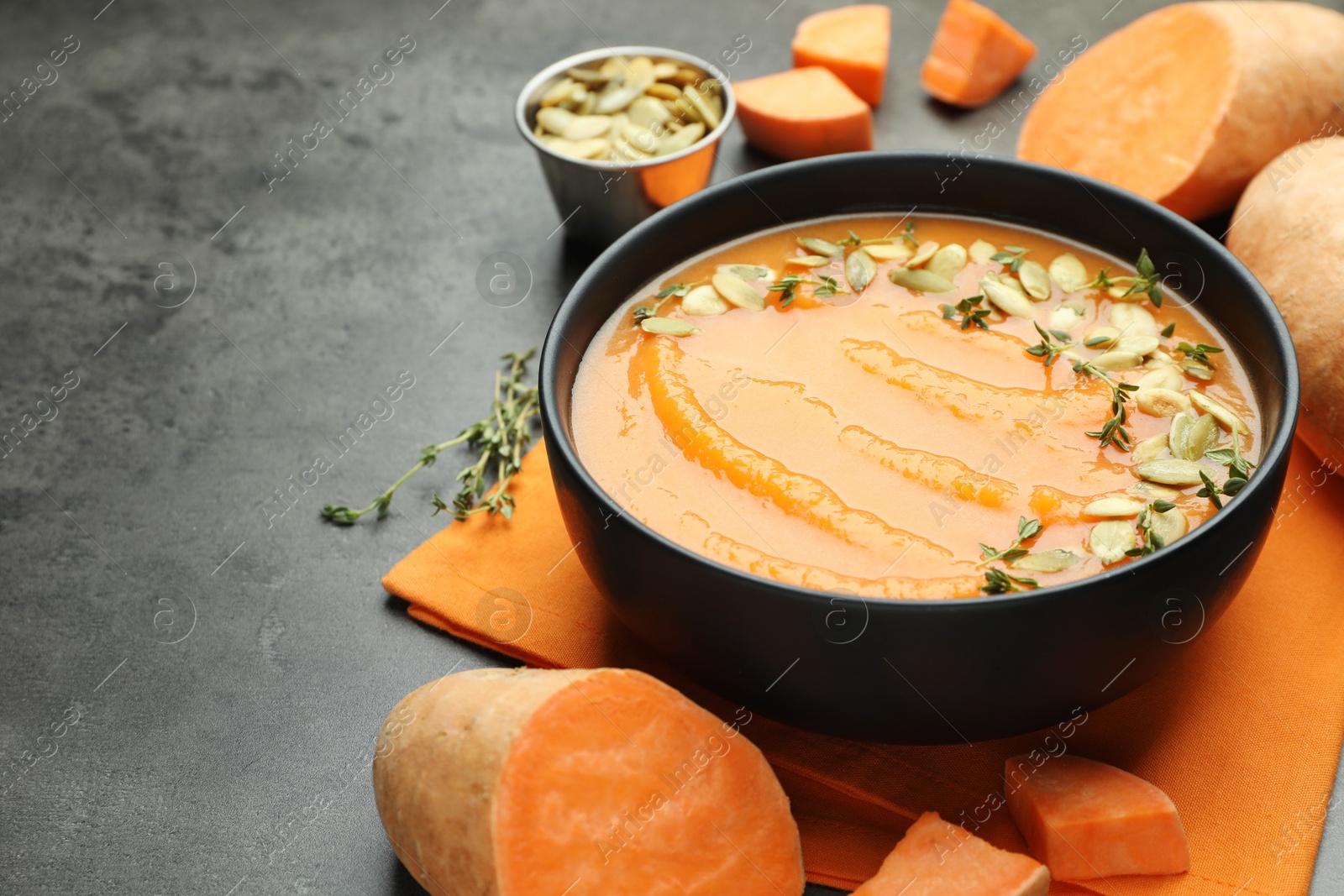 Photo of Delicious sweet potato soup with pumpkin seeds in bowl and vegetables on grey table, closeup. Space for text