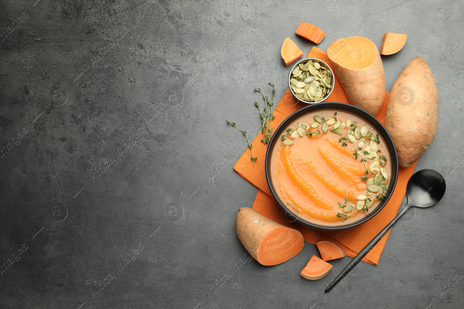 Photo of Delicious sweet potato soup with pumpkin seeds in bowl and vegetables on grey table, flat lay. Space for text