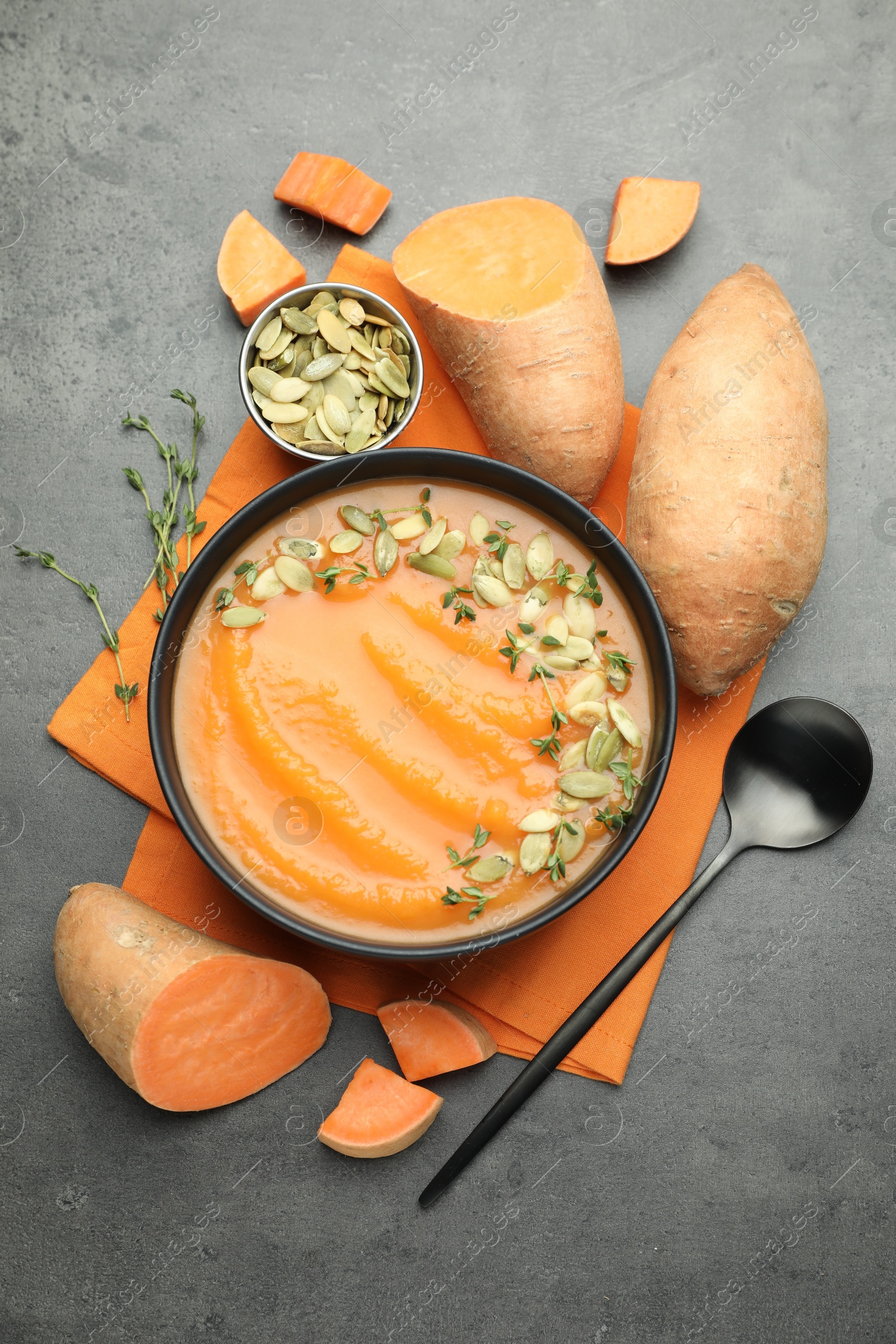 Delicious sweet potato soup with pumpkin seeds in bowl and vegetables on grey table, flat lay Photo of Delicious sweet potato soup with pumpkin seeds in bowl and vegetables on grey table, flat lay