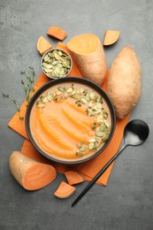 Photo of Delicious sweet potato soup with pumpkin seeds in bowl and vegetables on grey table, flat lay