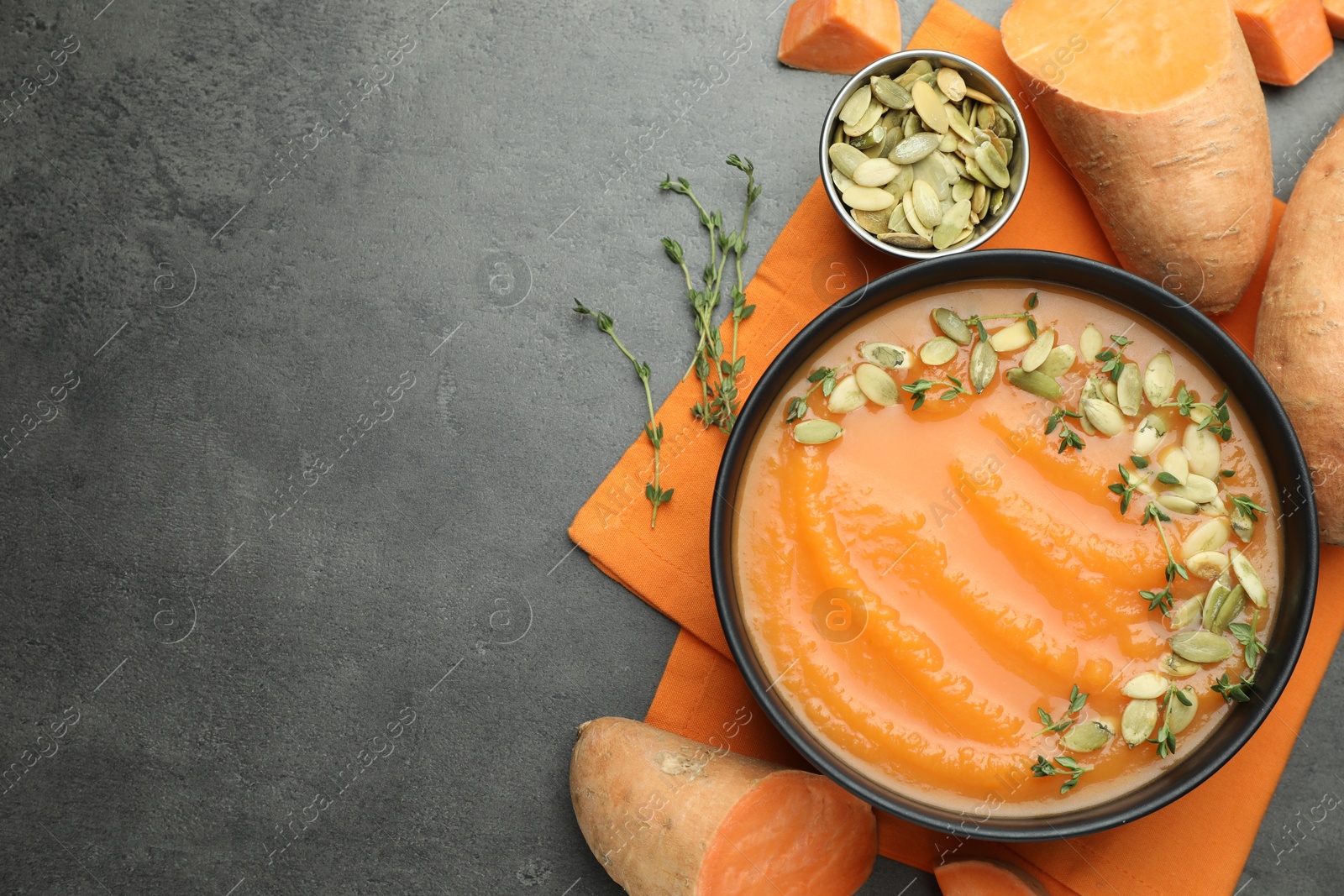 Photo of Delicious sweet potato soup with pumpkin seeds in bowl and vegetables on grey table, flat lay. Space for text