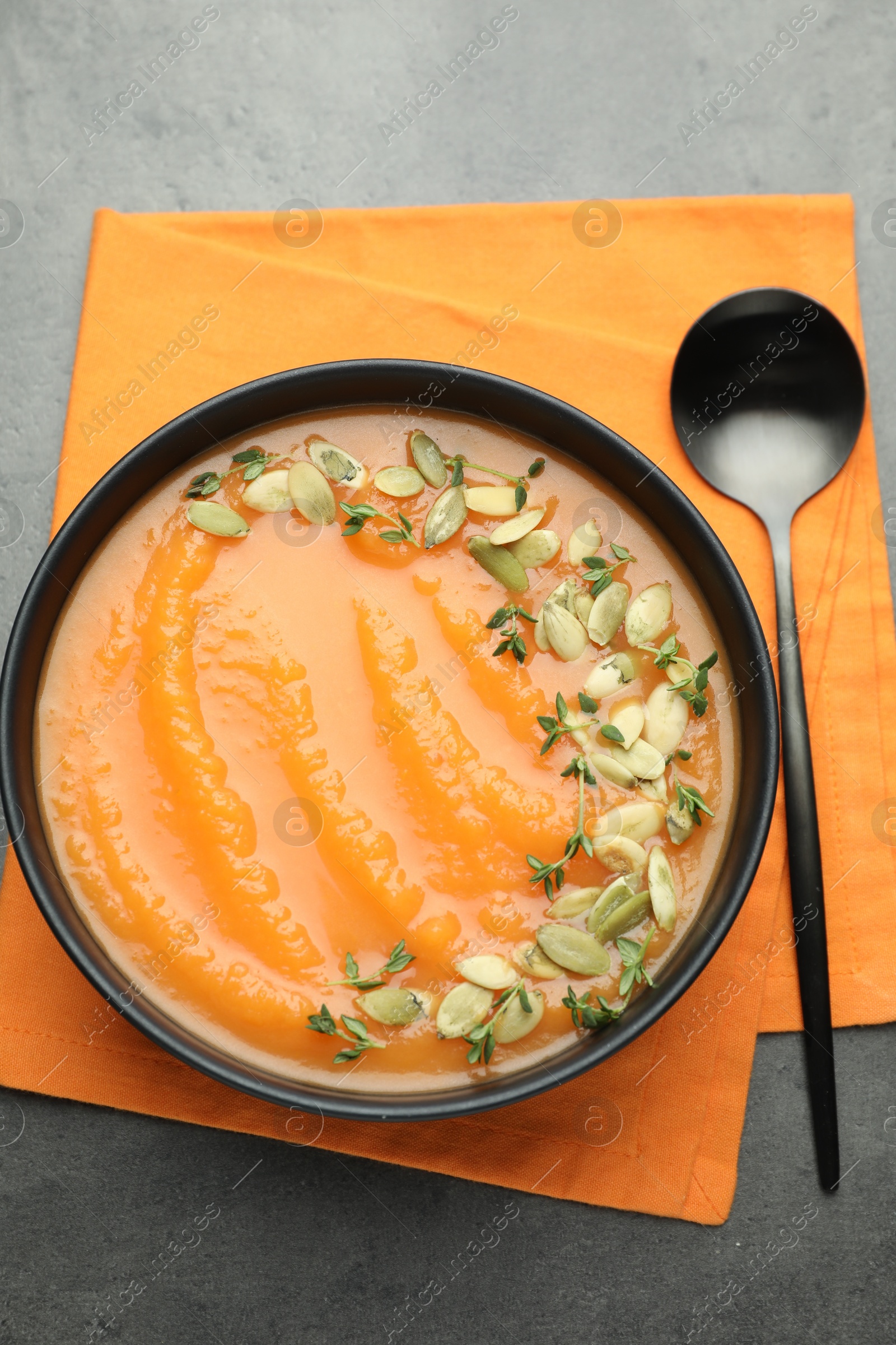 Photo of Delicious sweet potato soup with pumpkin seeds in bowl on grey table, top view