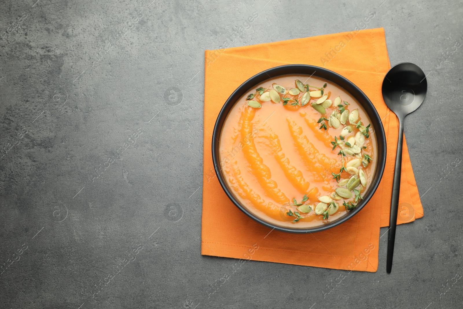 Photo of Delicious sweet potato soup with pumpkin seeds in bowl on grey table, top view. Space for text