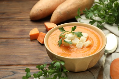 Photo of Delicious sweet potato soup with croutons in bowl, fresh vegetables and parsley on wooden table, closeup