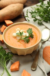 Photo of Delicious sweet potato soup with croutons in bowl, fresh vegetables and parsley on wooden table