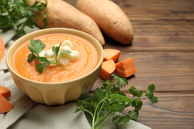 Photo of Delicious sweet potato soup with croutons in bowl, fresh vegetables and parsley on wooden table. Space for text