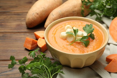 Photo of Delicious sweet potato soup with croutons in bowl, fresh vegetables and parsley on wooden table, closeup