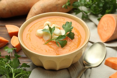 Photo of Delicious sweet potato soup with croutons in bowl, fresh vegetables and parsley on wooden table, closeup