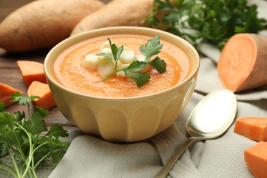 Photo of Delicious sweet potato soup with croutons in bowl, fresh vegetables and parsley on wooden table, closeup