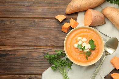 Photo of Delicious sweet potato soup with croutons in bowl, fresh vegetables and parsley on wooden table, flat lay. Space for text