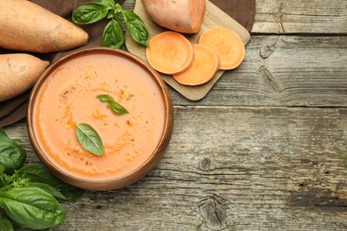 Photo of Delicious sweet potato soup with spices in bowl, fresh vegetables and basil on wooden table, flat lay. Space for text