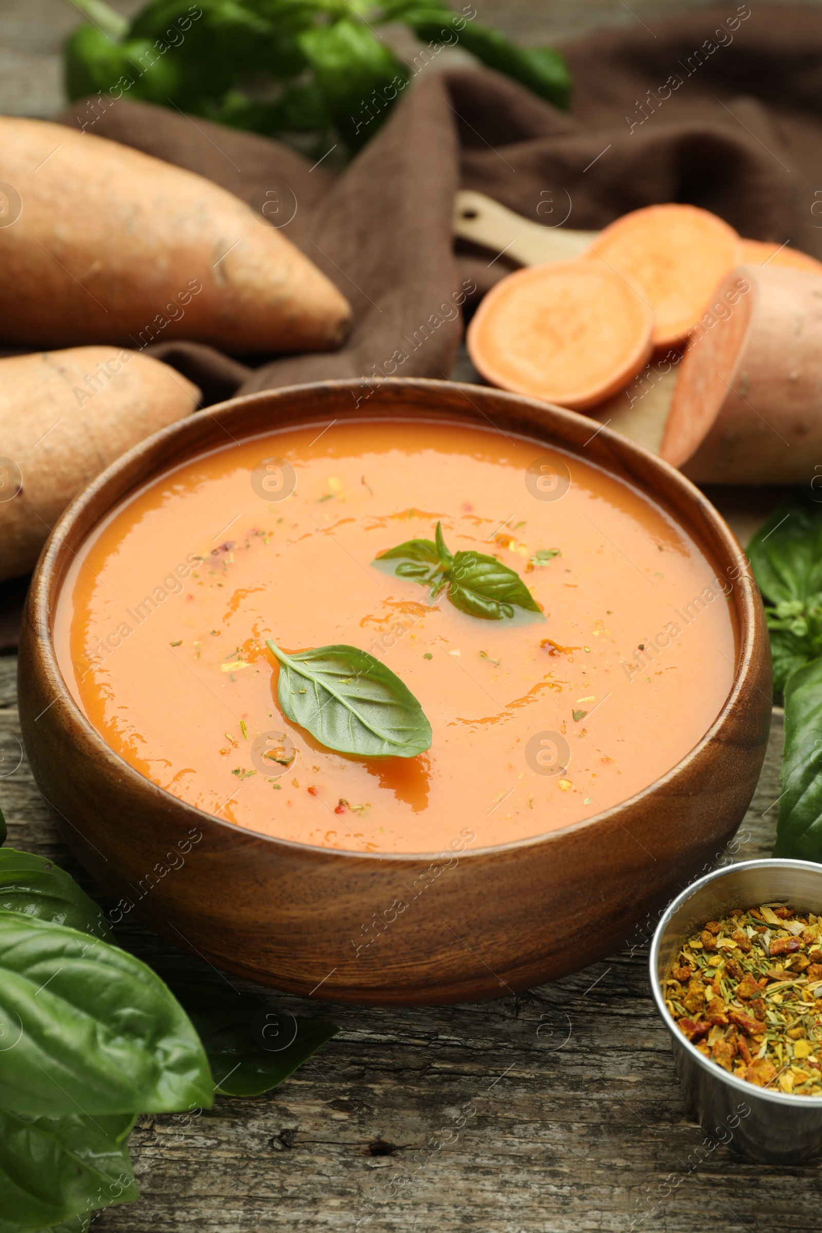 Delicious sweet potato soup with spices in bowl, fresh vegetables and basil on wooden table, closeup Photo of Delicious sweet potato soup with spices in bowl, fresh vegetables and basil on wooden table, closeup